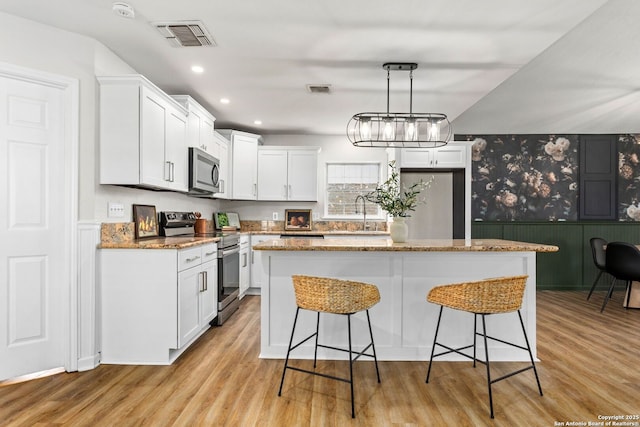 kitchen featuring light wood finished floors, visible vents, a breakfast bar area, stainless steel appliances, and white cabinetry