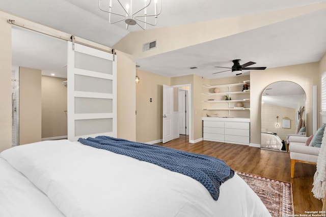 bedroom with visible vents, wood finished floors, a barn door, baseboards, and vaulted ceiling