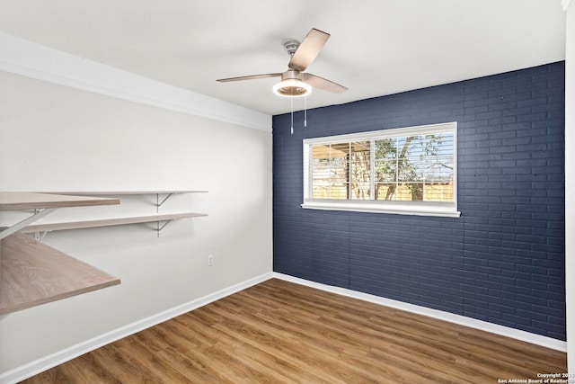 unfurnished room featuring brick wall, baseboards, ceiling fan, and wood finished floors