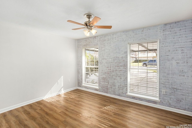 spare room with ceiling fan, brick wall, baseboards, and wood finished floors