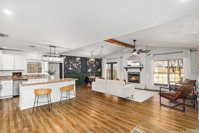 kitchen with lofted ceiling with beams, a kitchen island, stainless steel dishwasher, light wood-style floors, and a fireplace