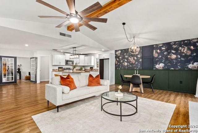 living area with visible vents, ceiling fan with notable chandelier, wood finished floors, and vaulted ceiling