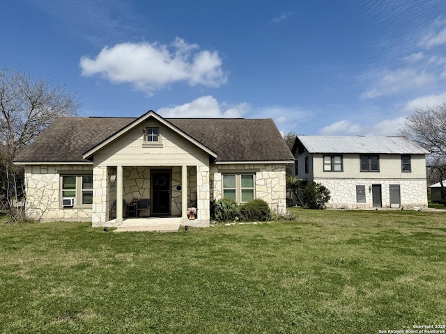 back of house featuring stone siding, a lawn, and a shingled roof