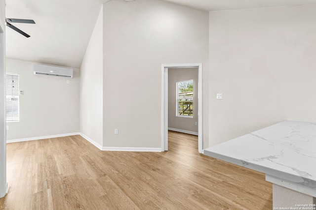 empty room with light wood-type flooring, high vaulted ceiling, a ceiling fan, a wall mounted AC, and baseboards