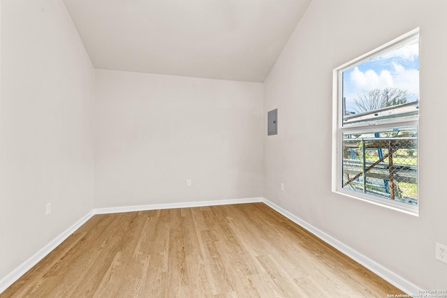 unfurnished room featuring electric panel, light wood-type flooring, baseboards, and vaulted ceiling