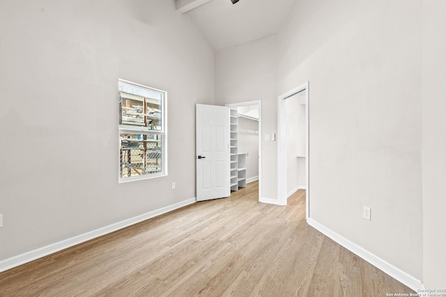 unfurnished bedroom with beam ceiling, high vaulted ceiling, light wood finished floors, baseboards, and a spacious closet