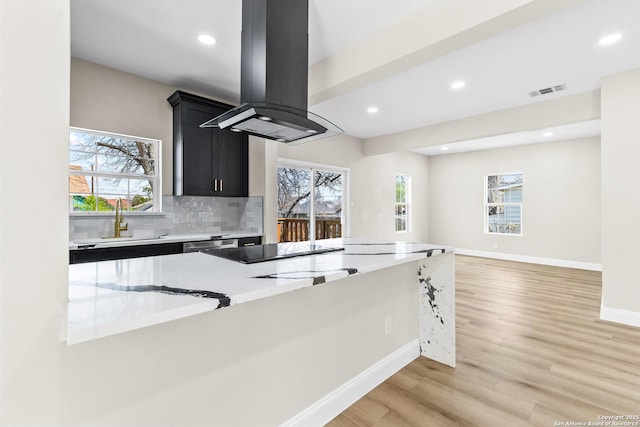 kitchen with a sink, decorative backsplash, island exhaust hood, light wood-style floors, and dark cabinets