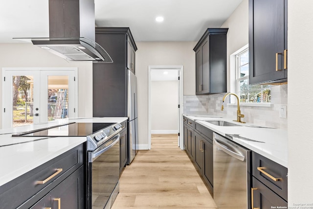 kitchen featuring light wood-type flooring, a sink, stainless steel appliances, island range hood, and decorative backsplash