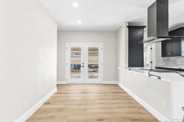 kitchen with light wood finished floors, tasteful backsplash, dark cabinetry, island range hood, and light countertops