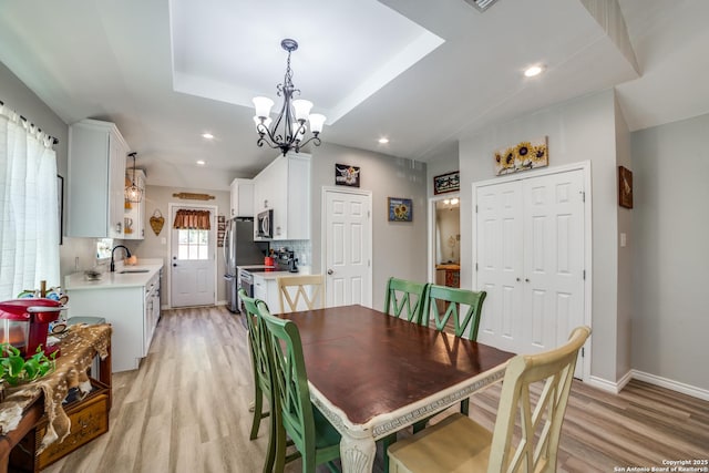 dining room with recessed lighting, light wood-style flooring, baseboards, and a tray ceiling