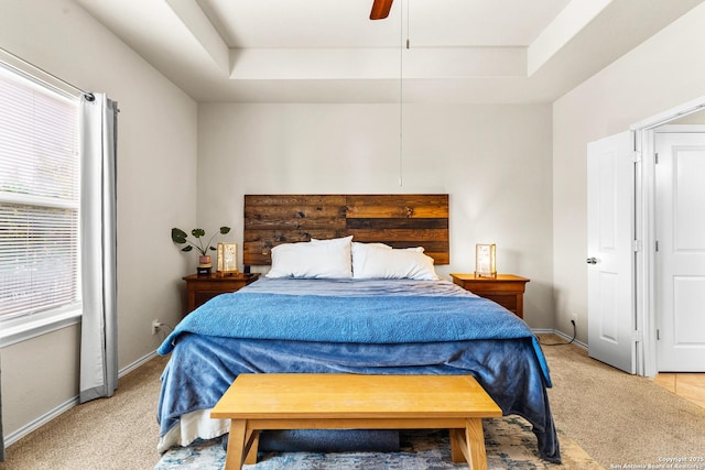 bedroom with light carpet, ceiling fan, baseboards, and a tray ceiling