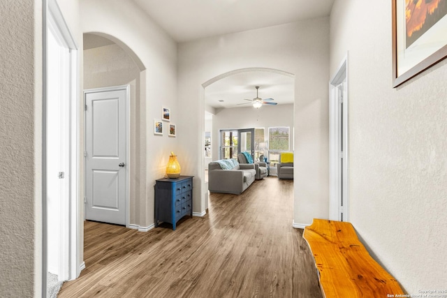 corridor with wood finished floors, arched walkways, and baseboards