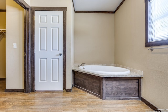 full bathroom featuring a garden tub, wood finished floors, baseboards, and ornamental molding