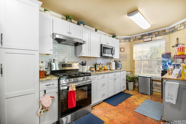 kitchen with under cabinet range hood, tasteful backsplash, appliances with stainless steel finishes, white cabinets, and light stone countertops