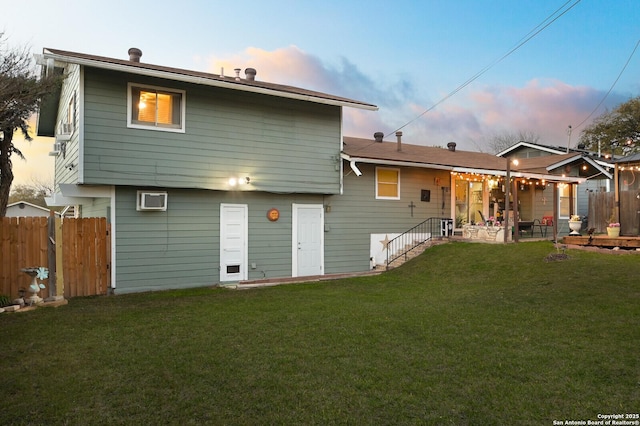 back of property at dusk with a patio area, a lawn, and fence