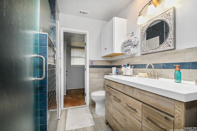 bathroom with visible vents, toilet, vanity, a stall shower, and tile walls