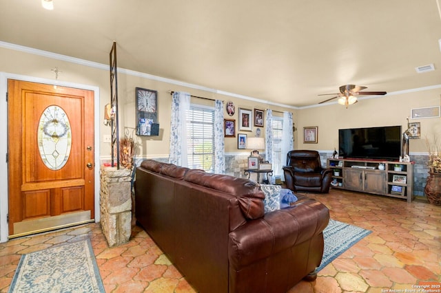 living area with crown molding, a ceiling fan, visible vents, and wainscoting