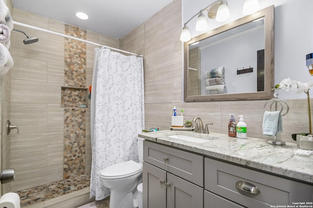 full bath with toilet, vanity, a tile shower, decorative backsplash, and tile walls