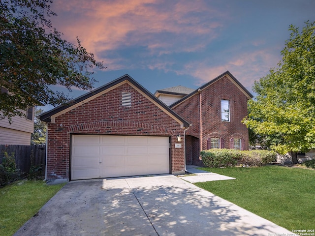 traditional-style house featuring fence, a yard, an attached garage, concrete driveway, and brick siding