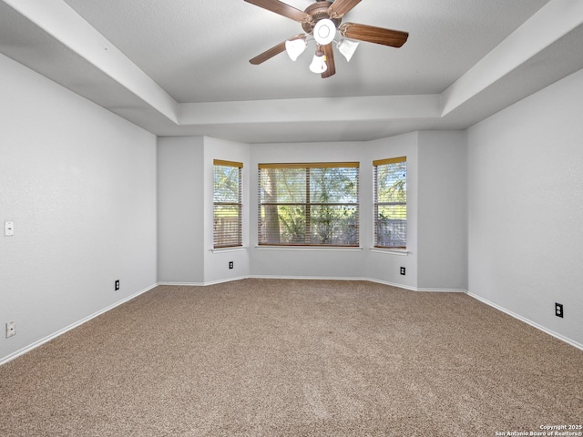 carpeted empty room with a raised ceiling, baseboards, and ceiling fan