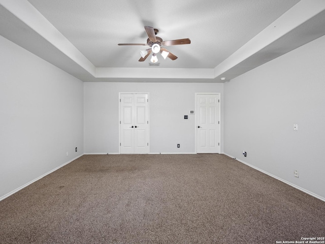 carpeted spare room featuring ceiling fan, baseboards, and a tray ceiling