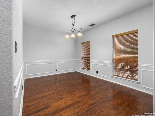 unfurnished room featuring a notable chandelier, visible vents, a decorative wall, and wood finished floors