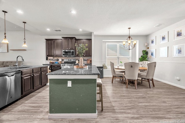 kitchen with dark brown cabinets, appliances with stainless steel finishes, light wood-type flooring, and a sink