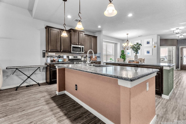 kitchen with dark brown cabinets, light wood-type flooring, decorative backsplash, stainless steel appliances, and a kitchen island with sink