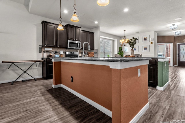 kitchen featuring dark wood finished floors, decorative backsplash, a center island with sink, and stainless steel appliances