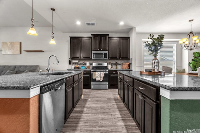 kitchen with wood finished floors, visible vents, a kitchen island with sink, a sink, and appliances with stainless steel finishes