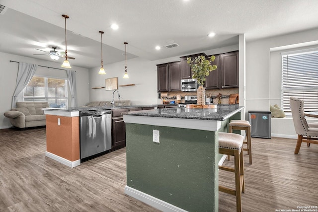 kitchen with a breakfast bar area, visible vents, dark brown cabinetry, appliances with stainless steel finishes, and light wood-type flooring