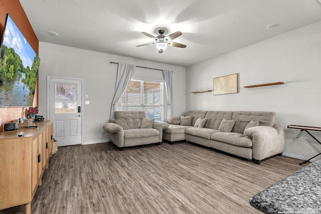 living room with a textured ceiling, wood finished floors, baseboards, and ceiling fan