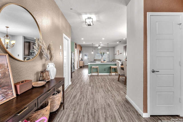 hallway featuring a notable chandelier, wood finished floors, baseboards, and a textured wall