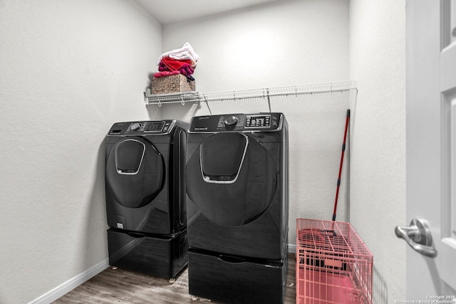 clothes washing area with laundry area, washing machine and dryer, baseboards, and wood finished floors