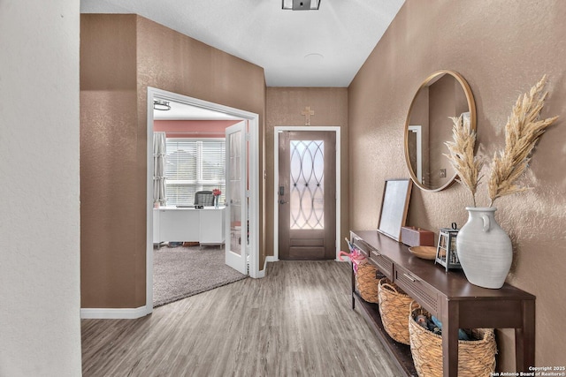 foyer featuring baseboards, wood finished floors, and a textured wall