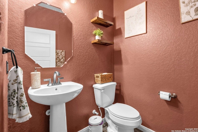 half bathroom with toilet, a textured wall, baseboards, and a sink