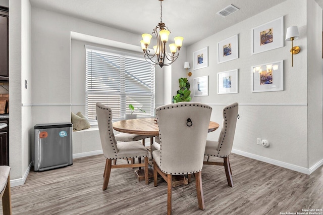 dining room featuring baseboards, visible vents, light wood-type flooring, and a chandelier