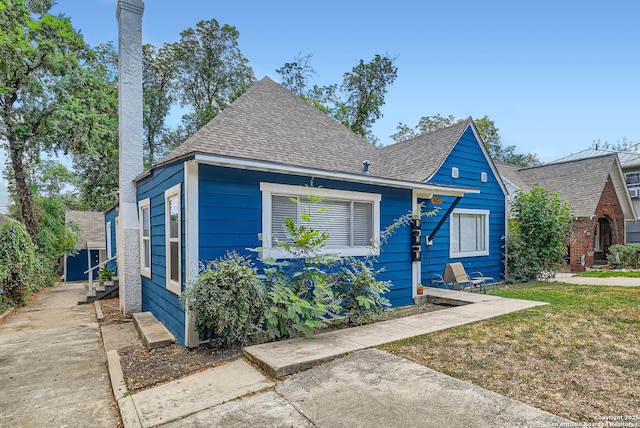 view of front facade with a shingled roof and a front yard