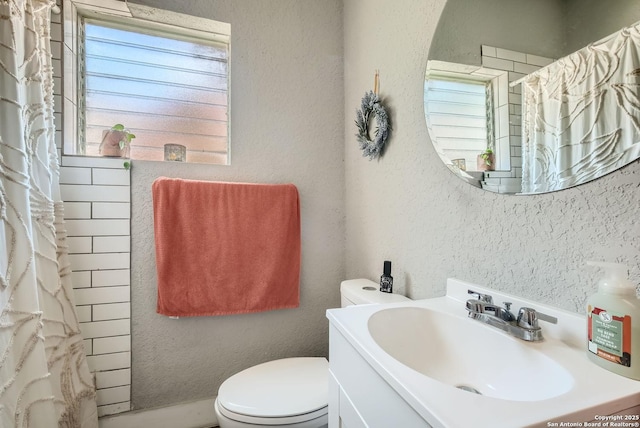 bathroom with vanity, curtained shower, toilet, and a textured wall