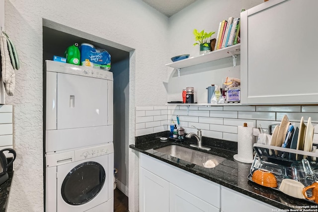 laundry area with a sink, a textured wall, laundry area, and stacked washer / dryer