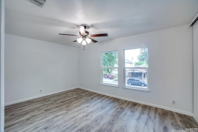 spare room with ceiling fan, visible vents, baseboards, and wood finished floors