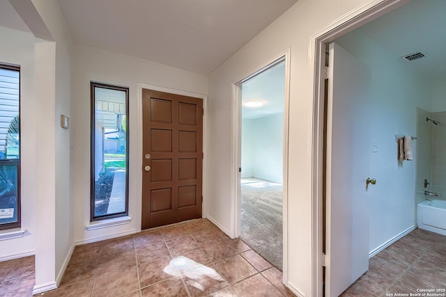 entryway featuring light tile patterned flooring, baseboards, visible vents, and light carpet