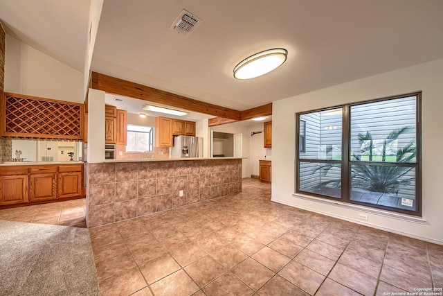 kitchen featuring light tile patterned floors, visible vents, appliances with stainless steel finishes, beamed ceiling, and brown cabinets