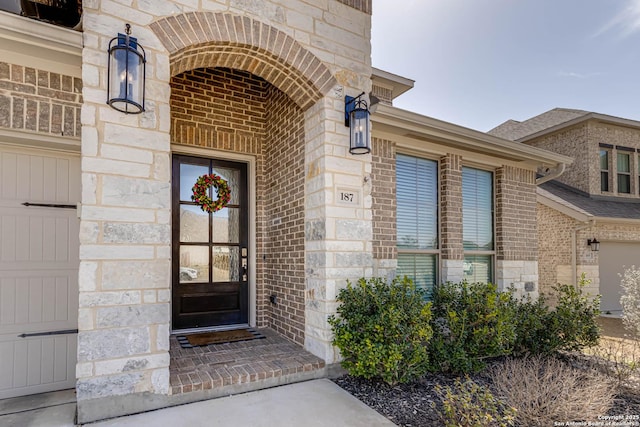 doorway to property with brick siding, stone siding, and a garage