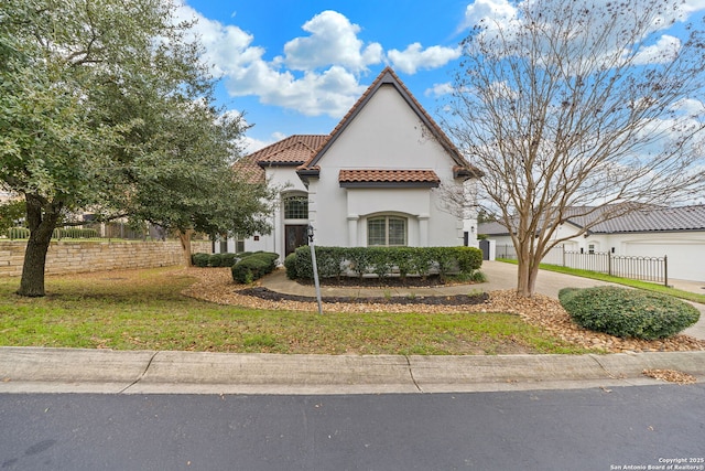 mediterranean / spanish house featuring a front lawn, fence, a tile roof, concrete driveway, and stucco siding