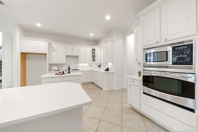 kitchen featuring tasteful backsplash, light countertops, light tile patterned floors, stainless steel appliances, and white cabinetry