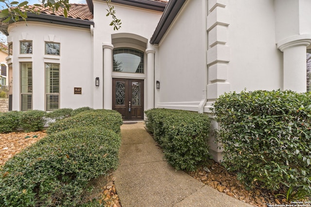 entrance to property featuring a tiled roof, french doors, and stucco siding