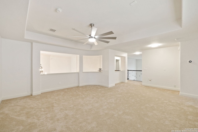 unfurnished room with visible vents, baseboards, ceiling fan, light carpet, and a raised ceiling