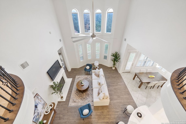 tiled living area featuring visible vents, baseboards, ceiling fan, stairs, and a towering ceiling