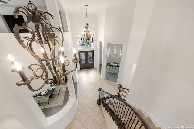 entryway featuring a towering ceiling, french doors, crown molding, light tile patterned floors, and a chandelier